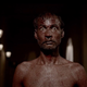 A shirtless man covered in blood drops stares with wide eyes in a scene from horror movie Kriya.